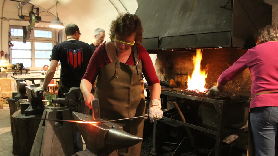 Erwachsene Teilnehmerin beim Schmieden von glühendem Metall